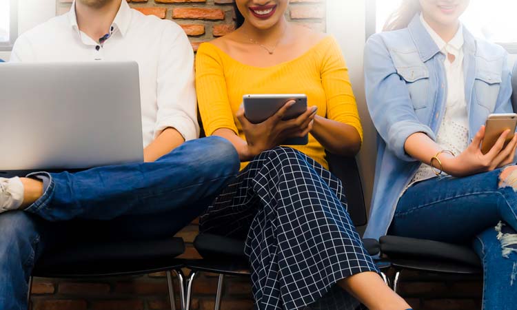 A group of people looking happy as they look down at their handheld electronic devices and laptop.