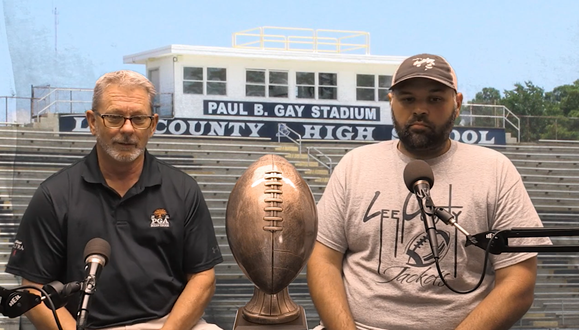 Sports host Keith Womack sits with Coach Burdeau with the Lee County High School football field in the background