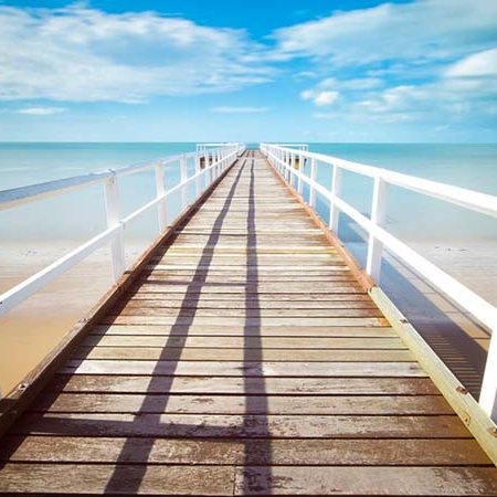 A bright day looking down to the end of a pier. The Pier stretches out into the ocean.